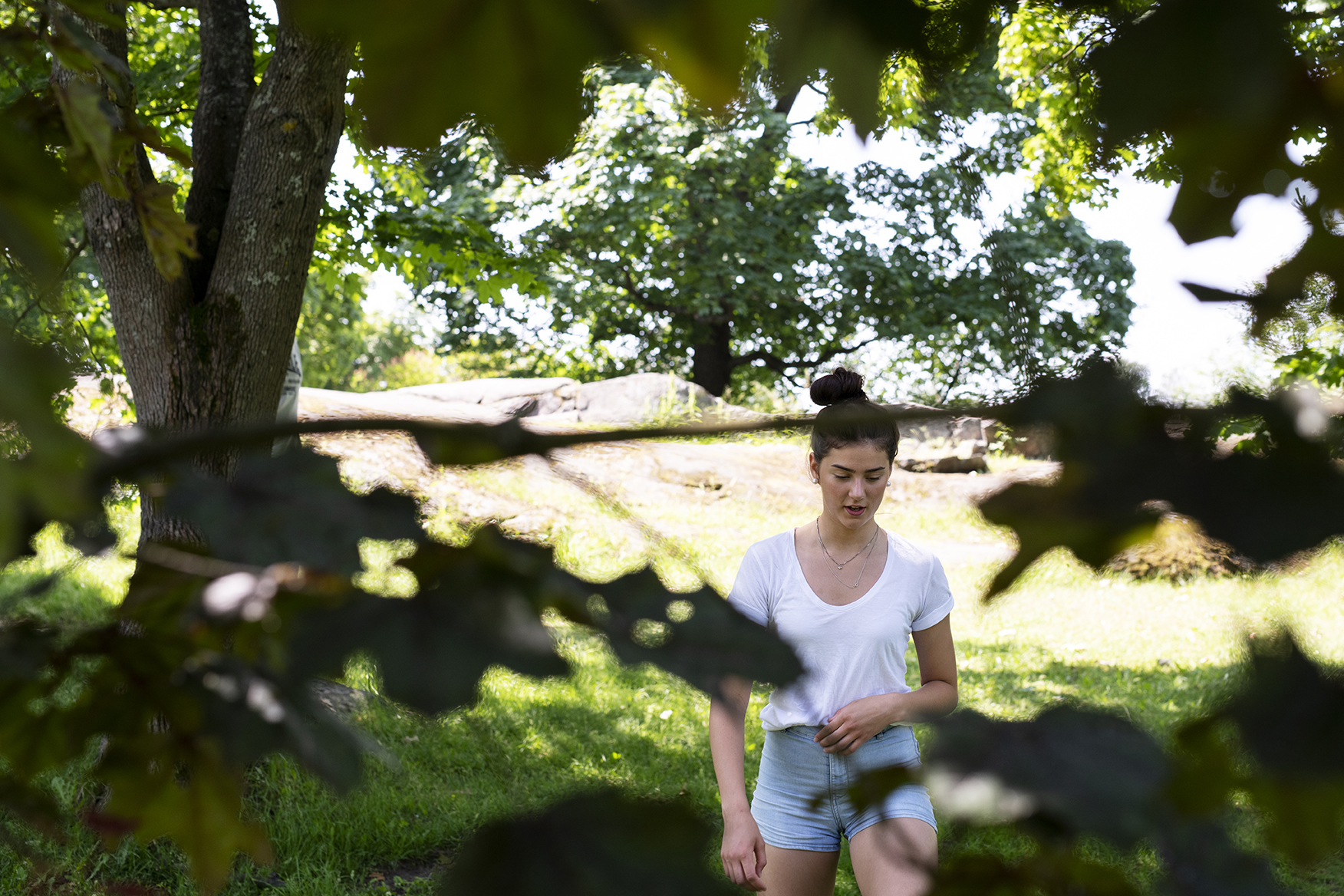 Tummahiuksinen tyttö, jolla on valkoinen t-paita ja shortsit kävelee kesäisessä puistossa.