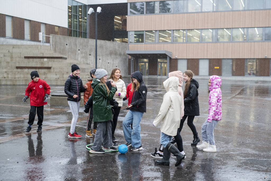 Lapsia kokoontuneina yhteen koulun pihalla sateisena päivänä.