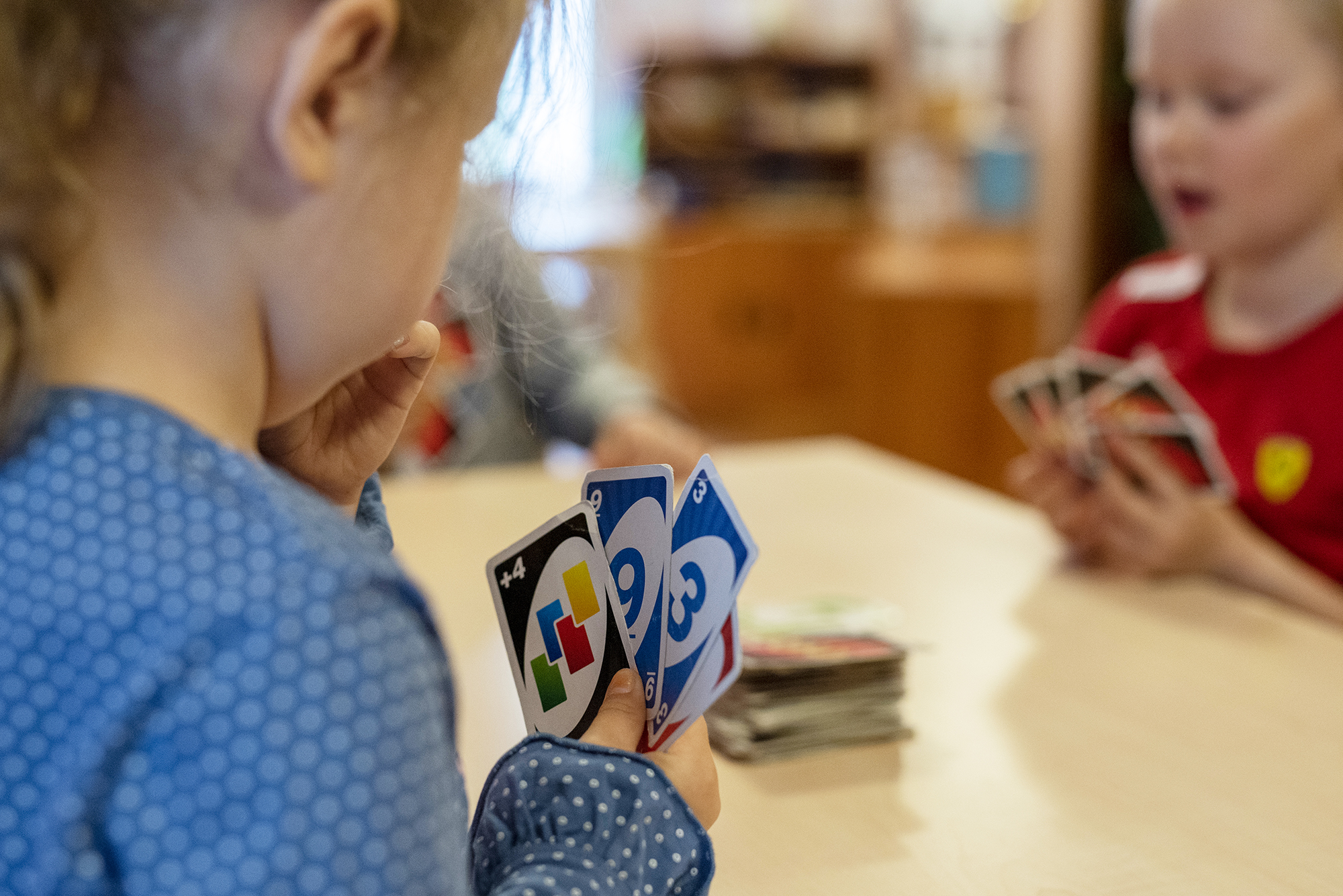 Lapset pelaavat Uno-pelikorteilla pöydän ääressä.