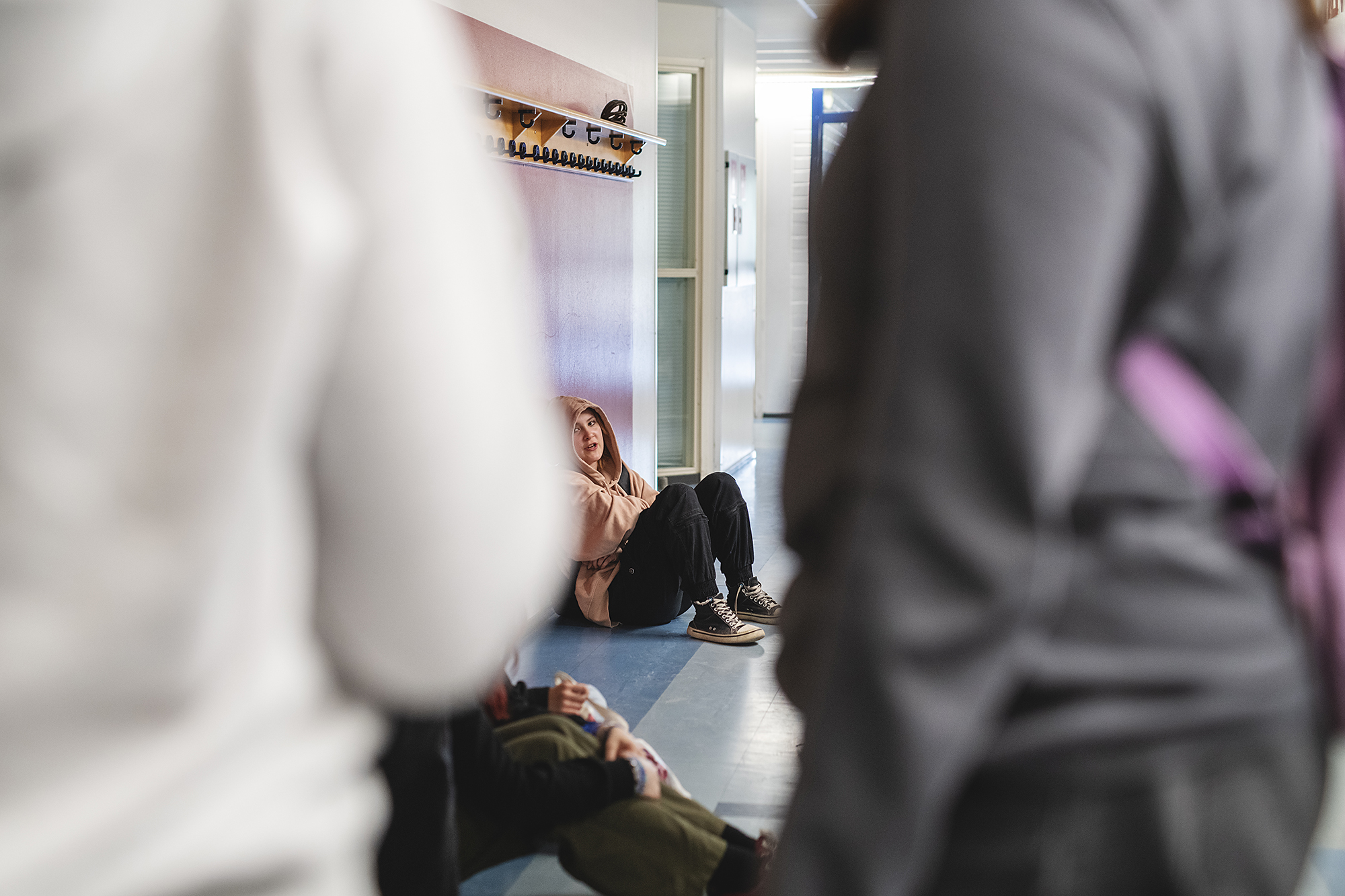Nuoria koulun käytävällä, yksi istumassa taustalla, kaksi selin etualalla.