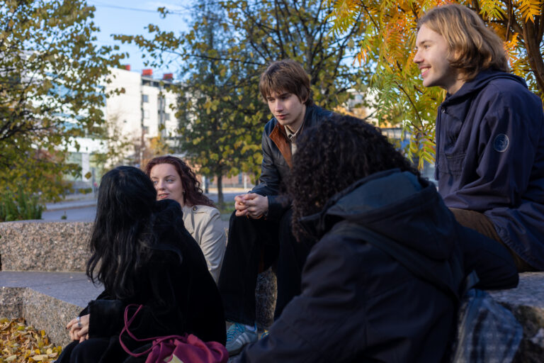 Joukko nuoria istuu kalliolla syksyllä