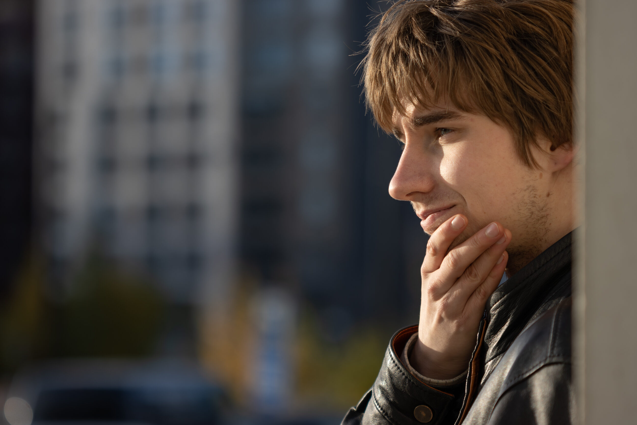 Nuori mies katsoo ilta-auringossa eteenpäin hymyillen, käsi leualla.