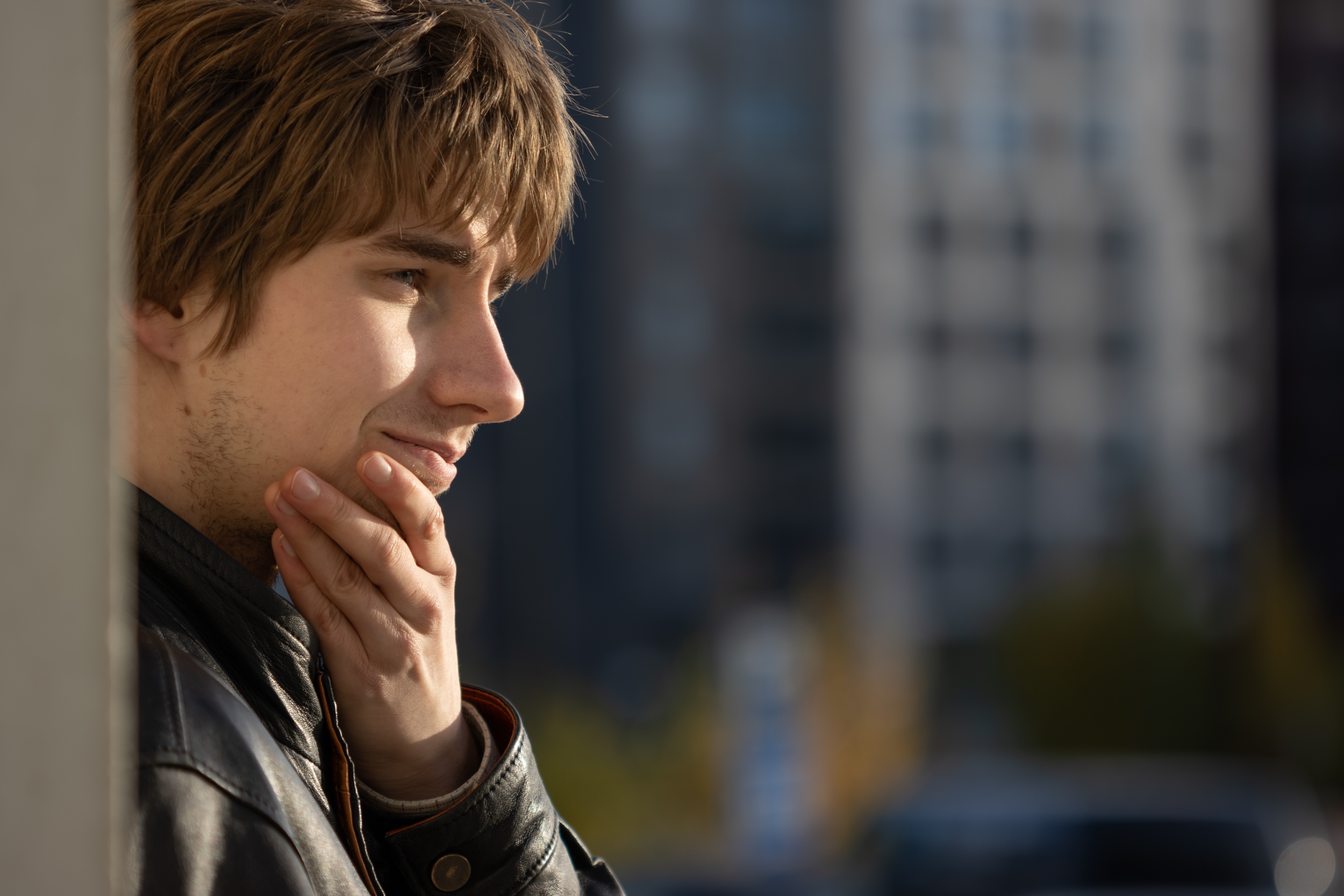 Nuori mies katsoo ilta-auringossa eteenpäin hymyillen, käsi leualla.