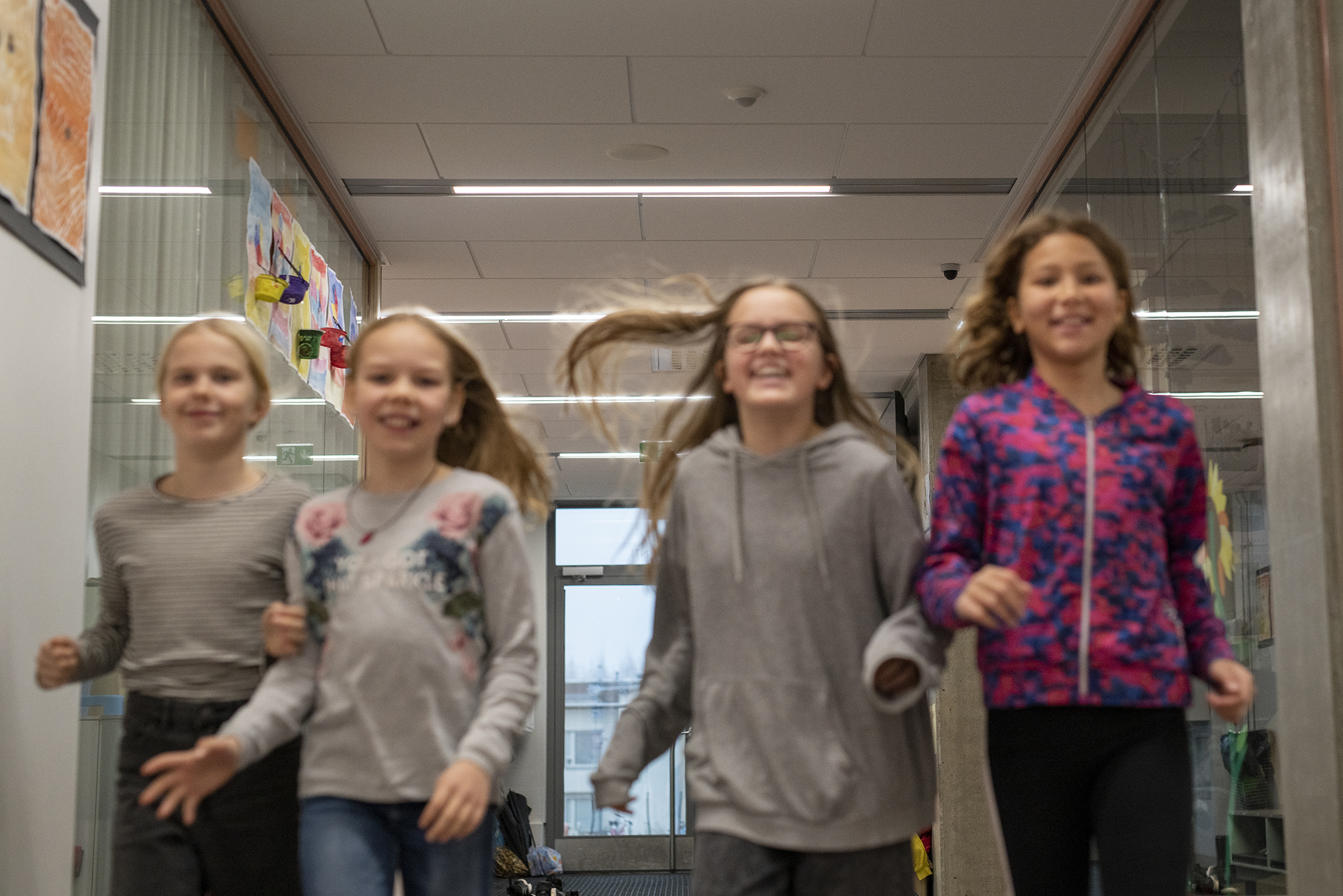 Neljä lasta juoksee iloisena koulun käytävällä