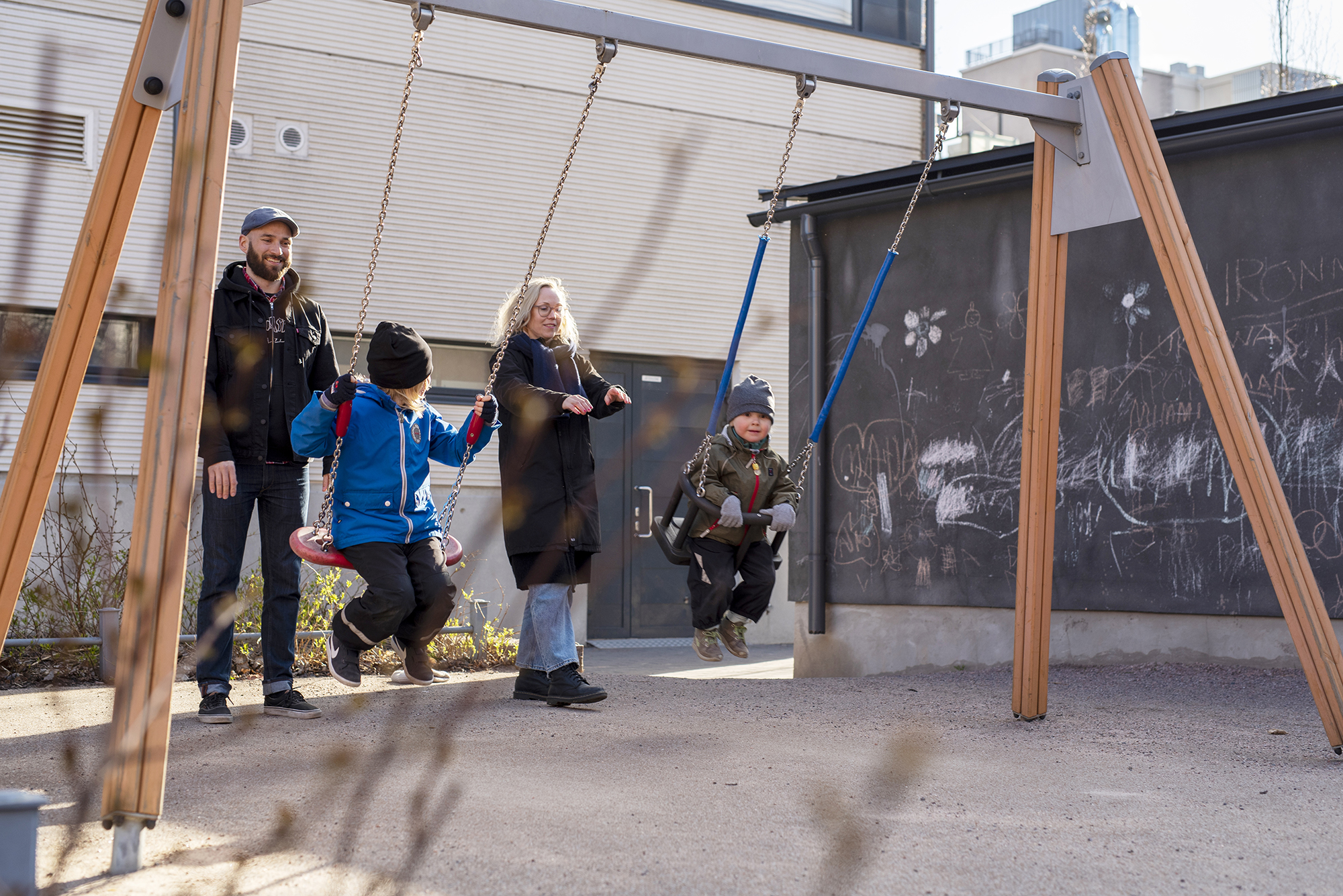 Kaksi lasta keinumassa, vanhemmat antavat vauhtia