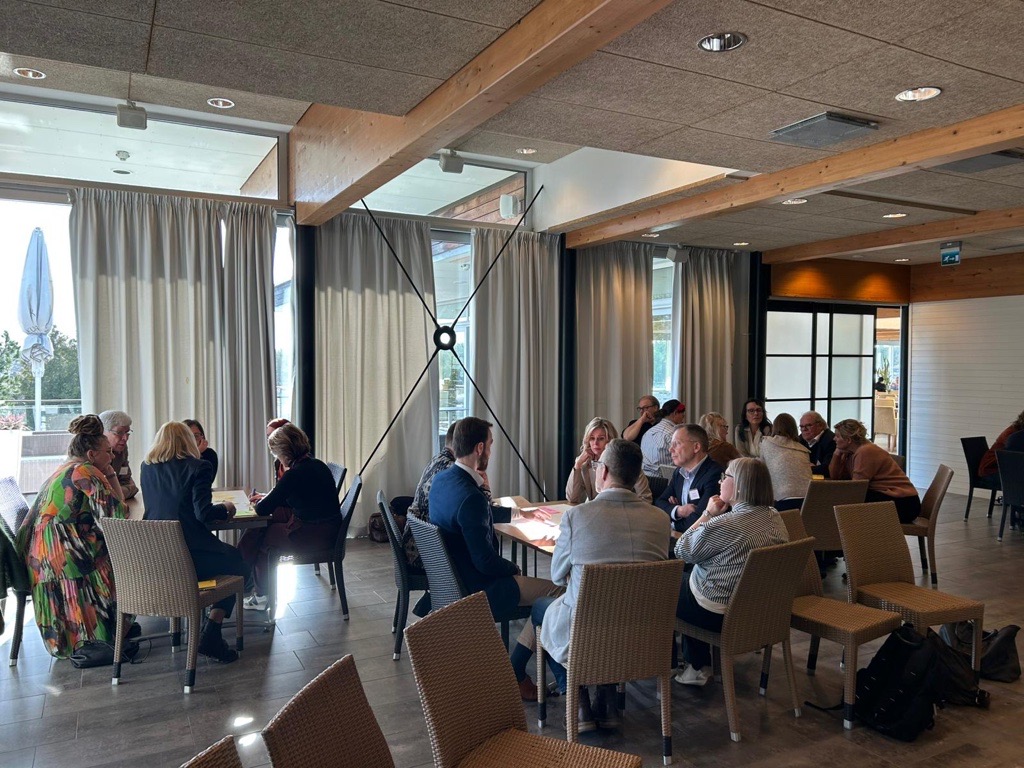 Ryhmä ihmisiä keskustelee pyöreän pöydän ääressä kokoustilassa. 